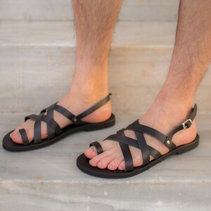May include: Dark brown leather sandals with crisscross straps and adjustable ankle straps. The sandals have a flat sole and are designed for comfort and style. Perfect for warm weather.