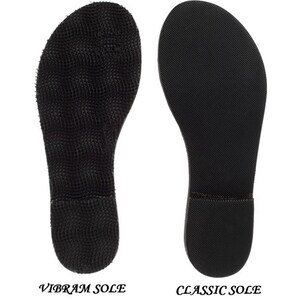 May include: Two black shoe soles are displayed side by side against a white background. The left sole is labeled "VIBRAM SOLE" and has a textured, grid-like pattern. The right sole, labeled "CLASSIC SOLE", has a smooth, slightly textured surface.