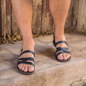 Op de afbeelding: Een paar zwarte leren sandalen met gekruiste banden. De sandalen hebben een eenvoudig ontwerp en zijn perfect voor warm weer.