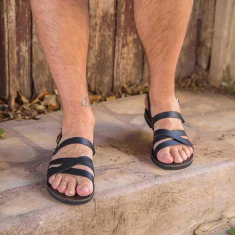 Op de afbeelding: Een paar zwarte leren sandalen met gekruiste banden. De sandalen hebben een eenvoudig ontwerp en zijn perfect voor warm weer.
