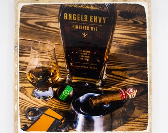 May include: A square image featuring a bottle of Angels Envy Finished Rye whiskey, a glass of whiskey, a cigar, an ashtray, a lighter, and a bottle cap. The items are arranged on a wooden surface. The bottle and glass are filled with amber liquid.