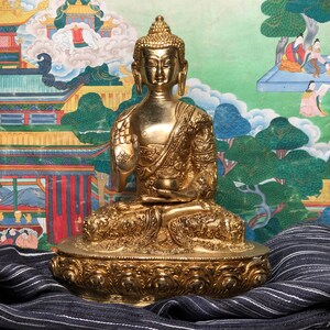 May include: A golden Buddha statue in a seated position, with intricate detailing on the robe and base. The statue is set against a backdrop of a colorful, traditional Asian-style painting. The Buddha is depicted with a serene expression.