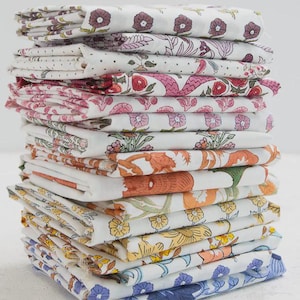 May include: A tall stack of folded fabric pieces, each featuring distinct floral and botanical patterns in various colors including purple, pink, orange, yellow, and blue on a white background, creating a layered textile display.