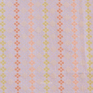 May include: A woven fabric featuring a repeating geometric pattern of vertical stripes in light purple, soft orange, and lime green on a pale pink background. The word FABLEISM is printed in small white letters near the bottom center of the textile.