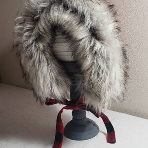 Puede incluir: Un gorro de piel sint&eacute;tica blanca con una cinta de cuadros rojos y negros atada alrededor.