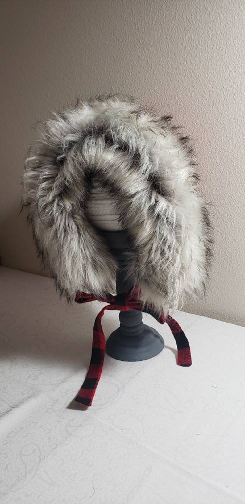 Puede incluir: Un gorro de piel sint&eacute;tica blanca con una cinta de cuadros rojos y negros atada alrededor.