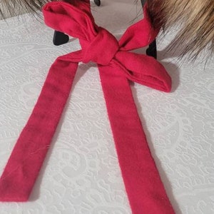 Puede incluir: Un lazo de tela rojo con un nudo en el centro. El lazo est&aacute; atado alrededor de un par de orejeras de piel marr&oacute;n.