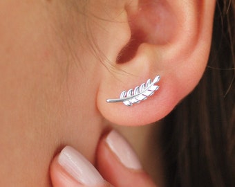 May include: A silver-toned ear climber earring shaped like a delicate fern leaf or feather. The earring features a curved, elongated design with small, segmented leaf-like details that follow the natural contour of the earlobe.