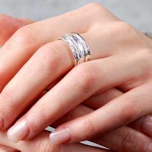 May include: A set of five silver stacking rings with a hammered finish. The rings are worn on a finger.