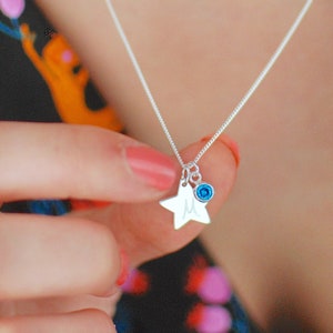 May include: A silver necklace with a star charm and a blue gemstone. The star charm has the letter "M" engraved on it.