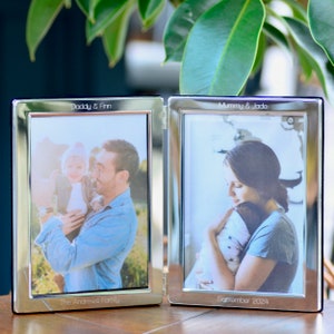 May include: Silver double photo frame with two photos of a family. The left photo shows a father holding a baby. The right photo shows a mother holding a baby. The top of the frame says "Daddy & Finn" and "Mummy & Jade". The bottom of the frame says "The Andrews Family" and "September 2024".