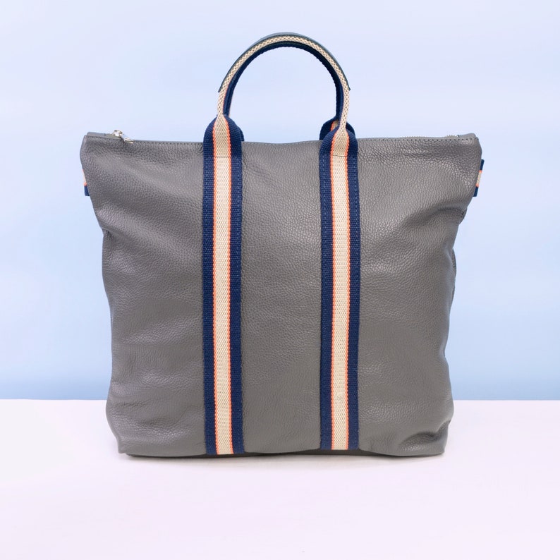 May include: A grey leather tote bag with navy blue and white striped straps.