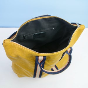 May include: A yellow leather tote bag with navy blue and white striped handles. The bag has a zipper closure and a small interior pocket.