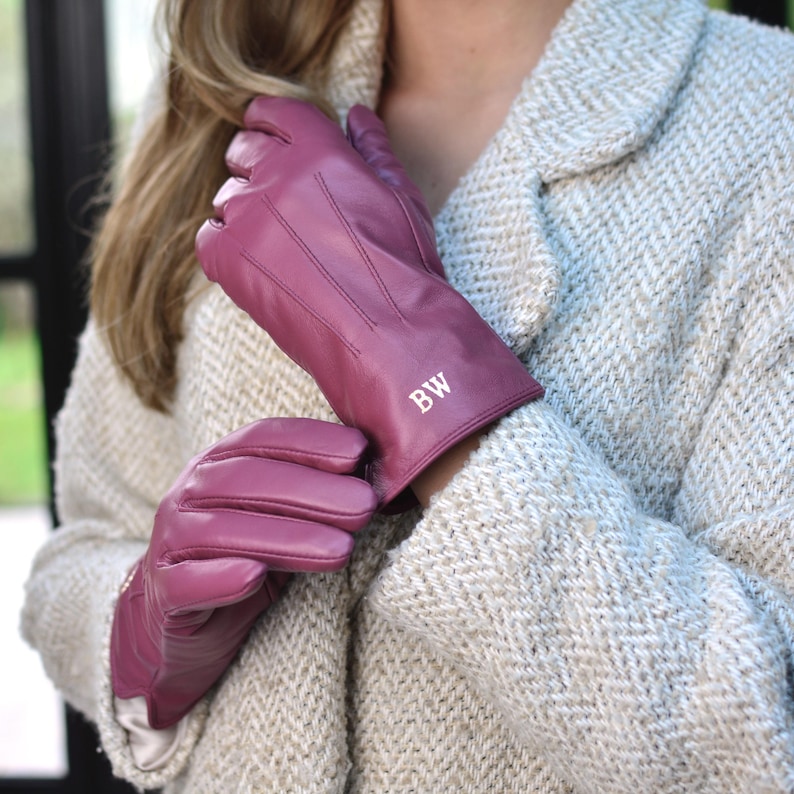 Peut inclure: Une paire de gants en cuir magenta avec les initiales "BW" en blanc sur le poignet. Les gants pr&eacute;sentent des coutures d&eacute;coratives et sont port&eacute;s avec un manteau en tweed clair.