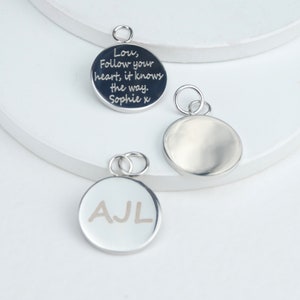 Silver circle shaped charms with engraving shown close up.