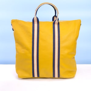 May include: A yellow leather tote bag with navy blue and white striped straps.