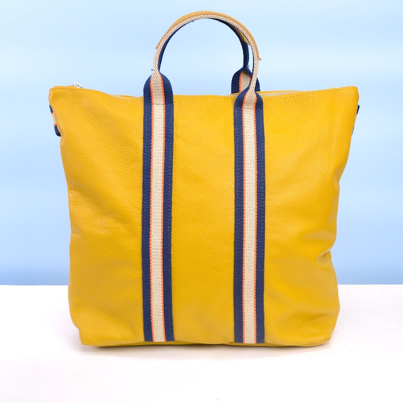May include: A yellow leather tote bag with navy blue and white striped straps.