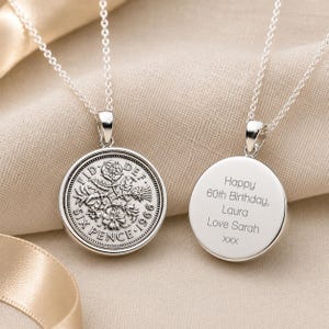 May include: Two silver coin pendants on fine chains. One pendant displays a floral design and the text "SIX PENCE 1966". The other pendant is engraved with "Happy 60th Birthday, Laura Love Sarah XXX".