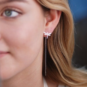 May include: Silver dangle earrings with a dragonfly design featuring clear cubic zirconia stones.
