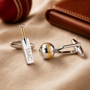 May include: A pair of silver-toned cufflinks featuring a cricket bat and a cricket ball. The bat has a gold-toned handle and the letters SMC engraved on the blade. The ball has a gold-toned seam detail. Each cufflink has a standard swivel toggle back.