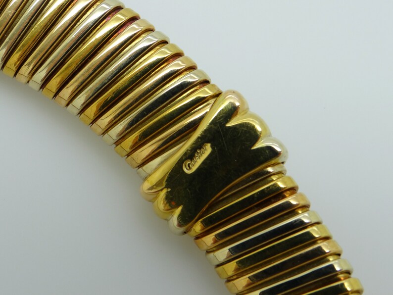 May include: A gold and silver bracelet with a ribbed design. The bracelet is marked with the word 'Cartier'.