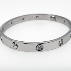 May include: A silver bangle bracelet with a screw closure and clear round stones set into the band.