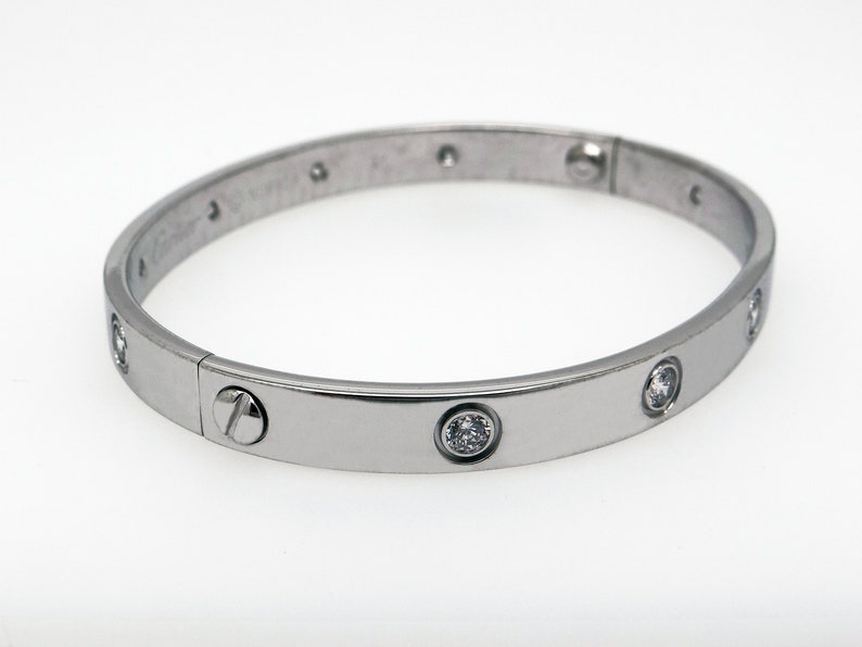 May include: A silver bangle bracelet with a screw closure and clear round stones set into the band.
