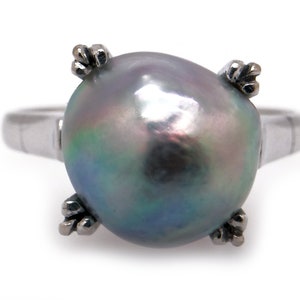 May include: A silver ring featuring a large, iridescent gray pearl. The pearl is held in place by four small, claw-like prongs. The ring band is a simple, polished silver. The pearl has a smooth, reflective surface with hints of green and blue.