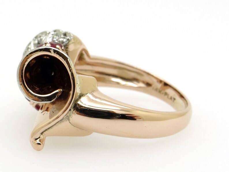 May include: A gold ring with a red and white stone set in a swirl design. The ring is marked "14K PLAT" on the inside of the band.