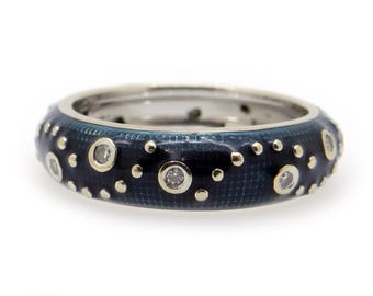 May include: A silver ring with a dark blue enamel band. The band is decorated with small gold dots and larger gold-rimmed clear stones. The ring is set against a white background.