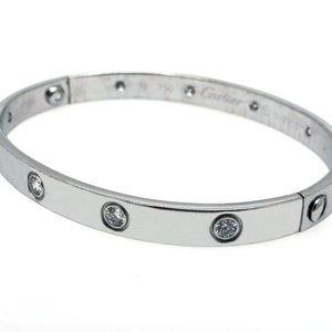 May include: A silver Cartier Love bracelet with five round diamonds set into the band. The bracelet is engraved with the Cartier logo and '750' on the inside.