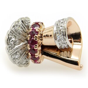 May include: A gold and silver earring with a cluster of small diamonds and a ring of red rubies. The earring is shaped like a small, curved horn.