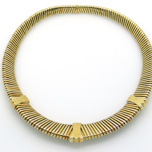 May include: A gold and silver toned necklace with a flexible, snake chain design. The necklace is made of multiple rows of linked metal strips.