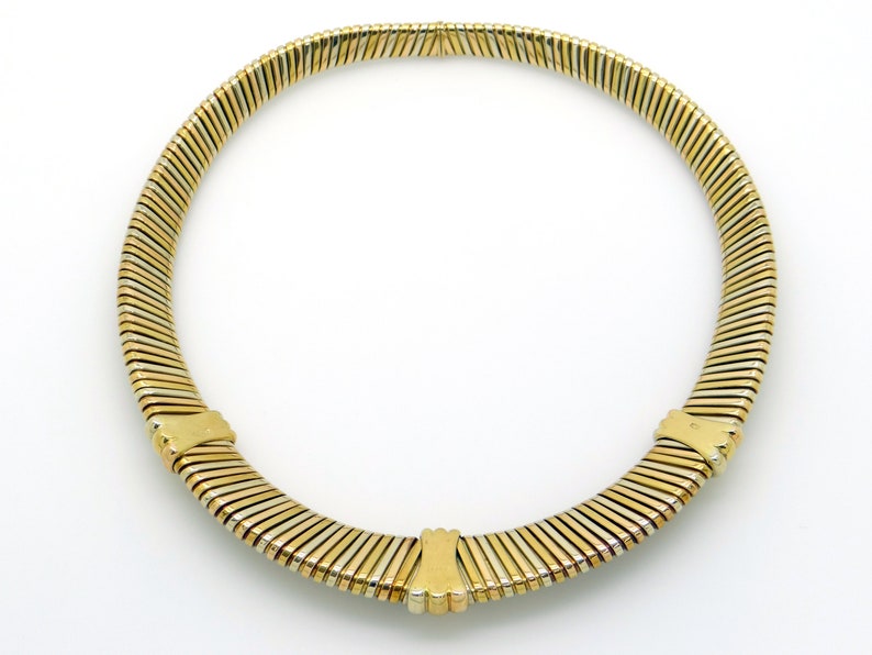 May include: A gold and silver toned necklace with a flexible, snake chain design. The necklace is made of multiple rows of linked metal strips.