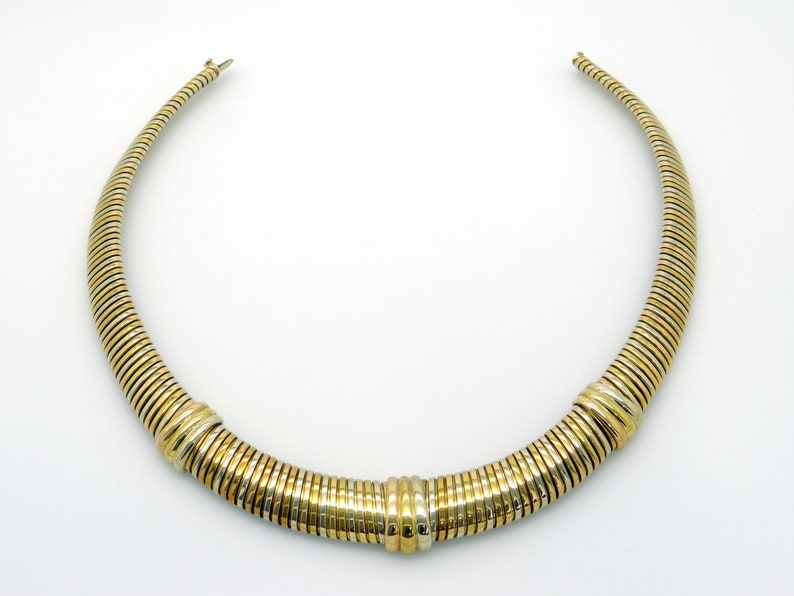 May include: A gold and silver toned necklace with a curved shape. The necklace is made of multiple small, stacked rings.