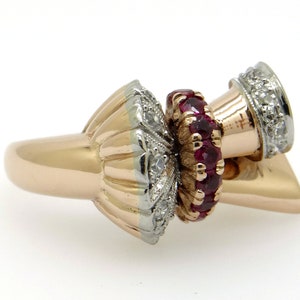 May include: A gold ring with a unique design featuring a cluster of red rubies and diamonds. The ring has a textured band and a three-dimensional design.