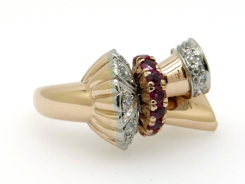 May include: A gold ring with a unique design featuring a cluster of red rubies and diamonds. The ring has a textured band and a three-dimensional design.