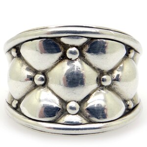 May include: A silver ring with a textured, quilted design. The ring has a wide band and a rounded shape.