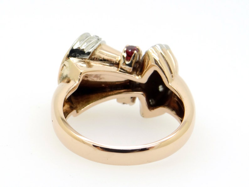 May include: A gold ring with a red gemstone and smaller white gemstones. The ring is set in a twisted design.