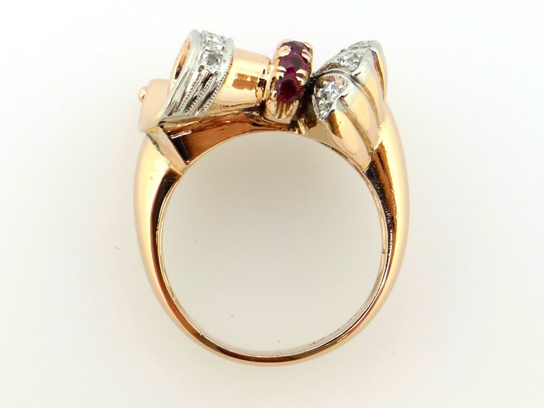 May include: A gold ring with a ruby and diamond setting. The ring is made of two-toned gold, with a white gold band and a rose gold setting. The setting features a cluster of rubies in the center, surrounded by a halo of diamonds.