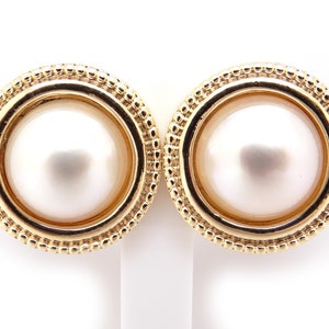 May include: A pair of gold earrings with a pearl in the center of each earring. The earrings have a beaded edge.
