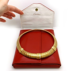 May include: A gold necklace with a coiled design in a red leather Cartier box. The box is open and the necklace is lying inside. The box has a white interior with the word 'Cartier' printed on it.