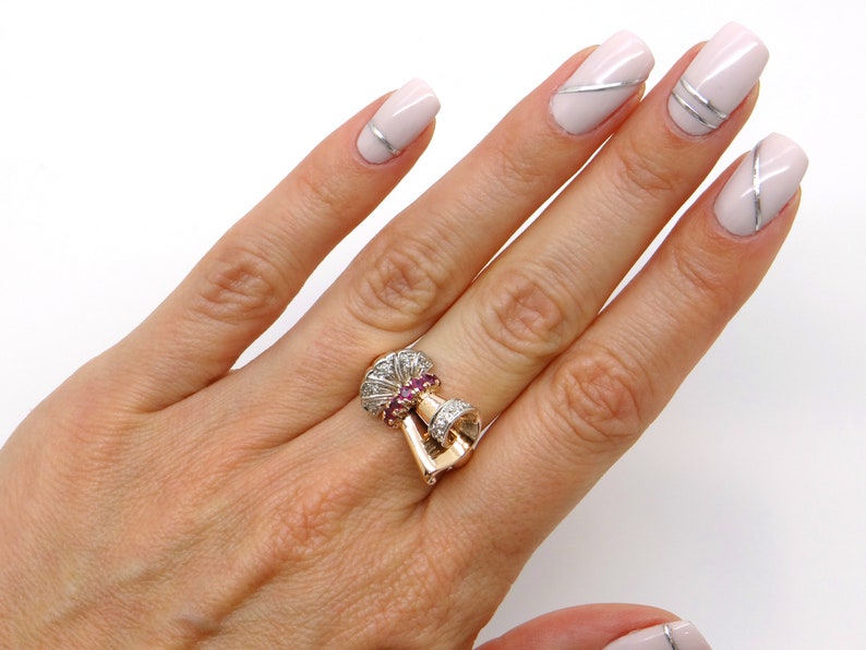 May include: A gold ring with a large, ornate design featuring a cluster of pink gemstones surrounded by smaller white gemstones.