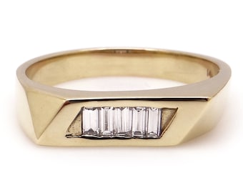 May include: A gold band ring with a row of five baguette-cut diamonds set in the center.