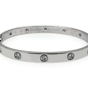 May include: A silver Cartier Love bracelet with diamonds. The bracelet is inscribed with 'Cartier' and '18 750' on the inside.