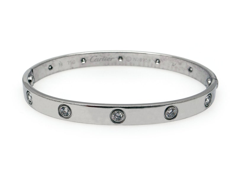 May include: A silver Cartier Love bracelet with diamonds. The bracelet is inscribed with 'Cartier' and '18 750' on the inside.