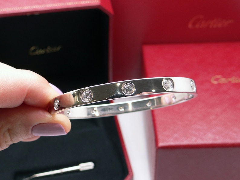 May include: A silver Cartier Love bracelet with five diamonds set in the band.
