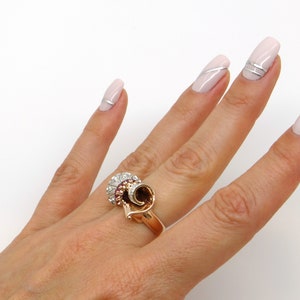 May include: A gold ring with a swirl design and a cluster of red and white stones.