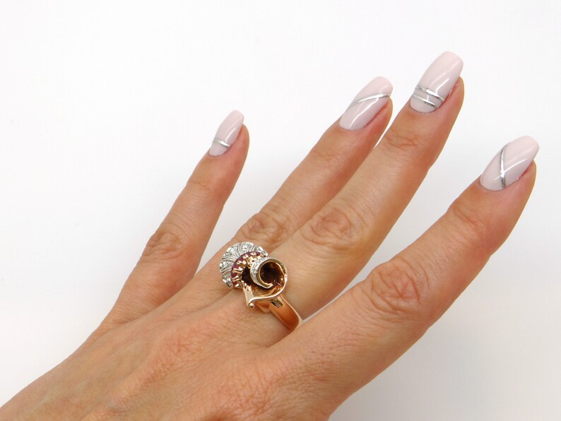 May include: A gold ring with a swirl design and a cluster of red and white stones.