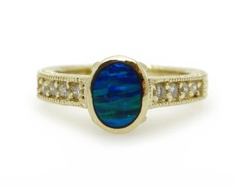 May include: A gold ring featuring an oval-shaped opal with vibrant blue and green hues. The band is adorned with small, clear gemstones and intricate detailing. A beautiful piece of jewelry.